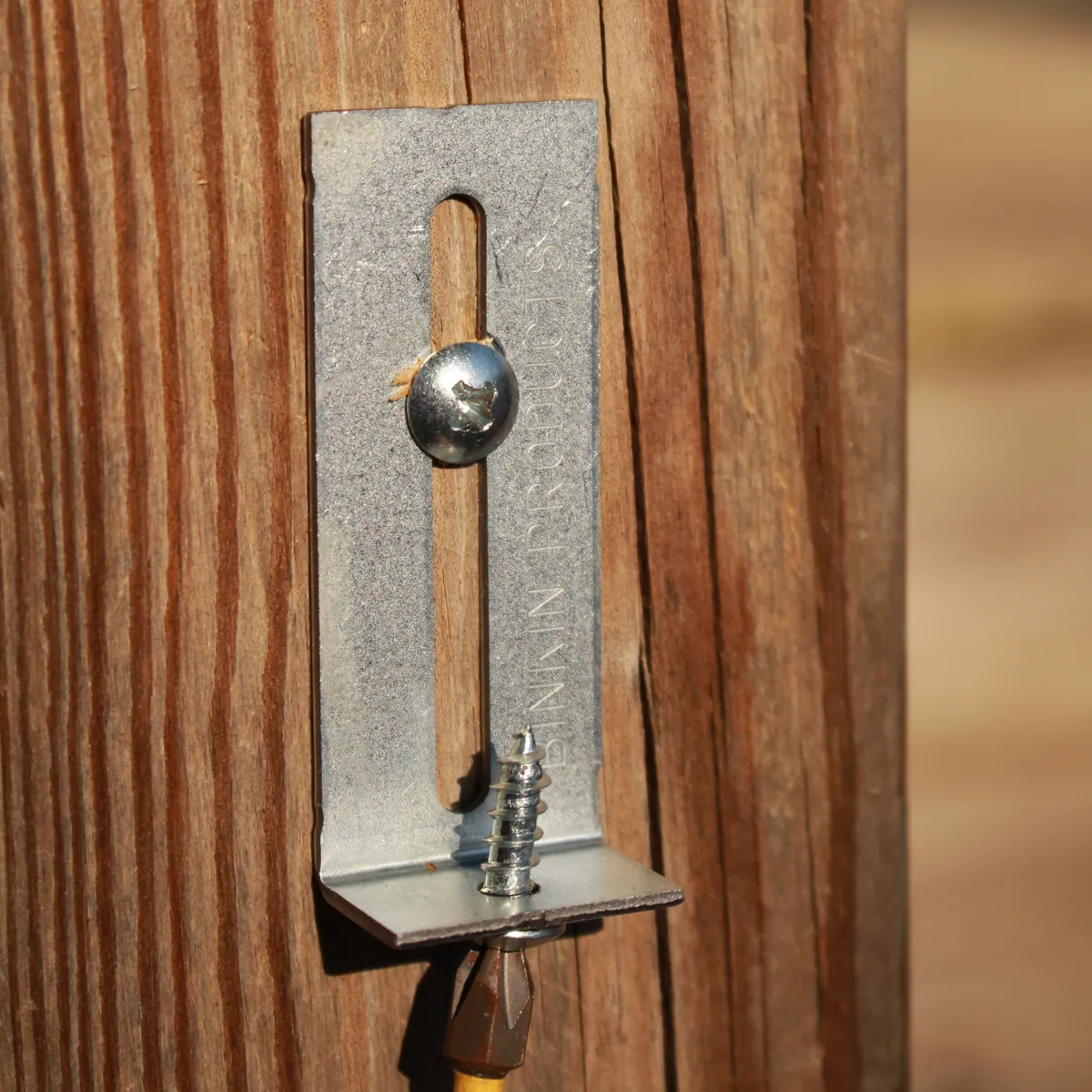 A BINKIN bracket on a wooden fence post, the slotted leg upright with a screw in the slot